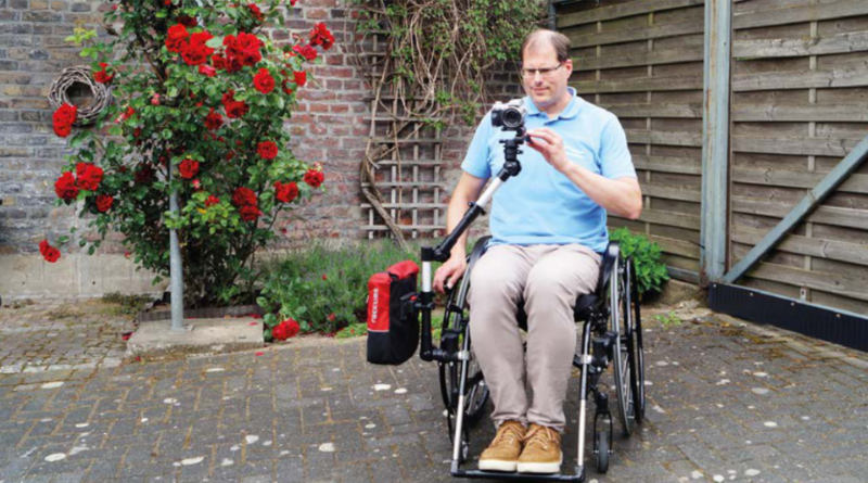 Mann im Rollstuhl mit einer angebrachten Kamera mit Stativ